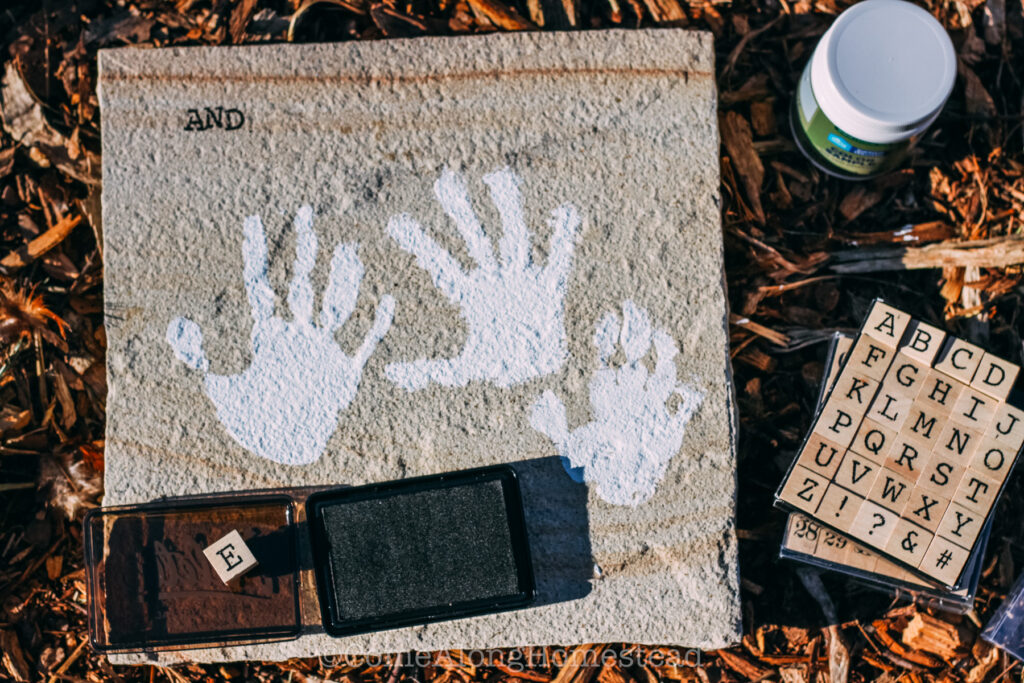 image of three white handprints on a paver with partial letters and an ink pad and ink pad letters