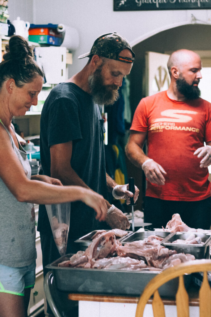 Three people butchering chickens inside a kitchen.