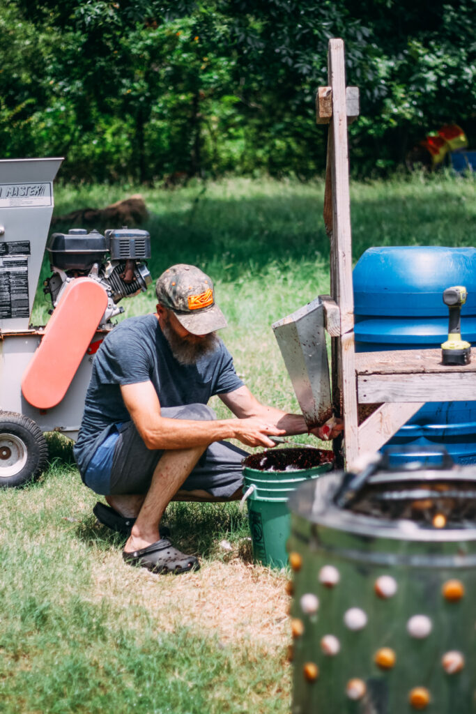 Man working at a chicken kill cone station with a kill cone and bucket underneath to catch blood during butchering.